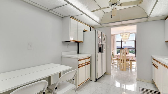 kitchen featuring pendant lighting, ceiling fan with notable chandelier, a paneled ceiling, white cabinetry, and white refrigerator with ice dispenser