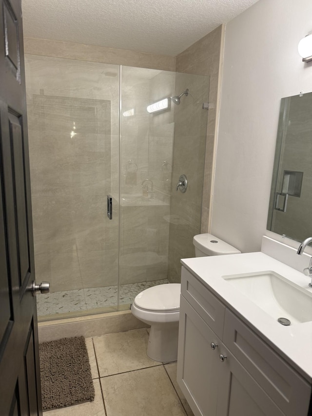 bathroom featuring toilet, a shower with shower door, a textured ceiling, vanity, and tile patterned flooring