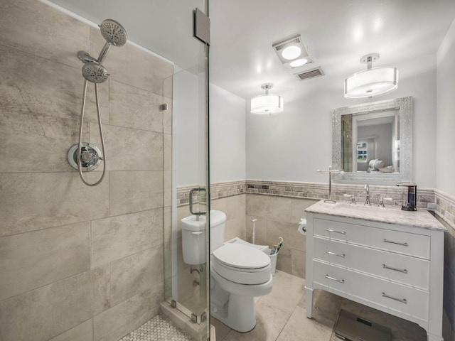 bathroom featuring tile walls, a tile shower, vanity, tile patterned floors, and toilet