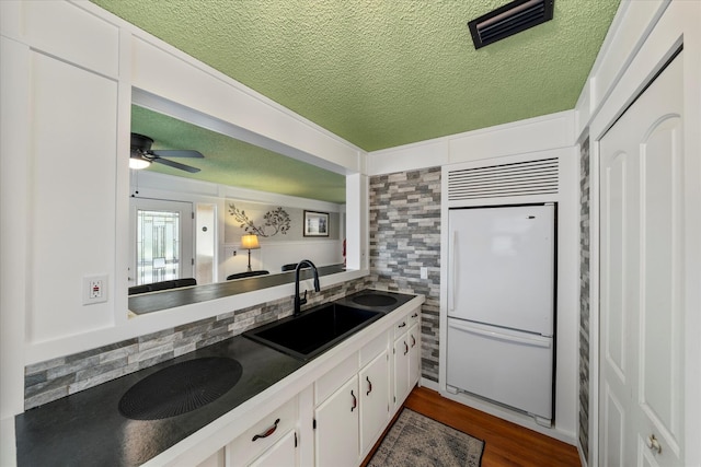 kitchen with sink, a textured ceiling, white built in fridge, hardwood / wood-style flooring, and white cabinets