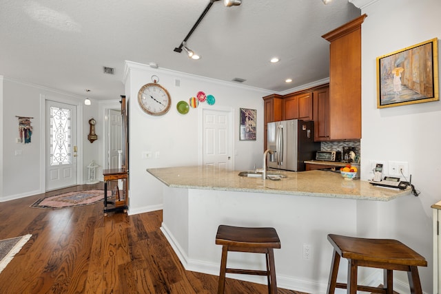 kitchen with sink, a breakfast bar, light stone counters, stainless steel fridge with ice dispenser, and kitchen peninsula