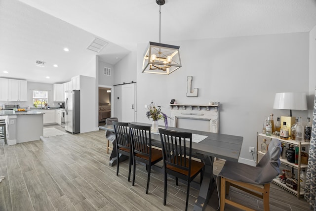 dining space with lofted ceiling, a notable chandelier, light hardwood / wood-style flooring, and a barn door