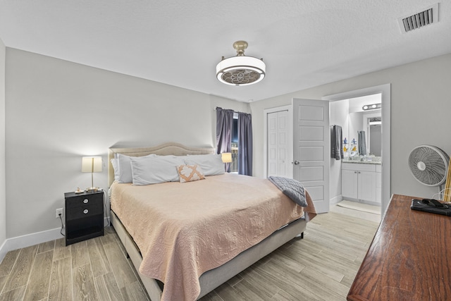 bedroom with ensuite bath, light hardwood / wood-style floors, a closet, and a textured ceiling