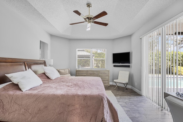 bedroom with ceiling fan, access to exterior, a raised ceiling, and a textured ceiling