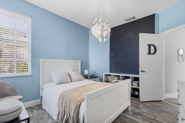 bedroom with dark wood-type flooring, a textured ceiling, and a notable chandelier