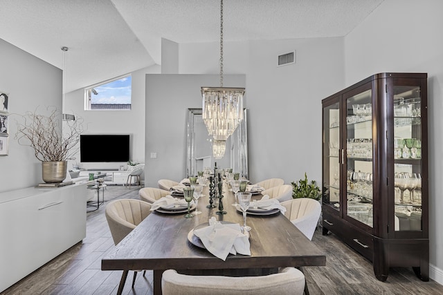 dining room featuring a notable chandelier, lofted ceiling, wood-type flooring, and a textured ceiling