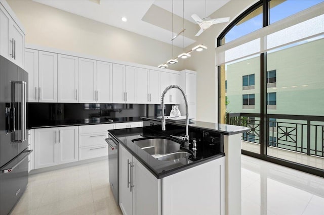 kitchen with high quality fridge, white cabinetry, an island with sink, sink, and hanging light fixtures