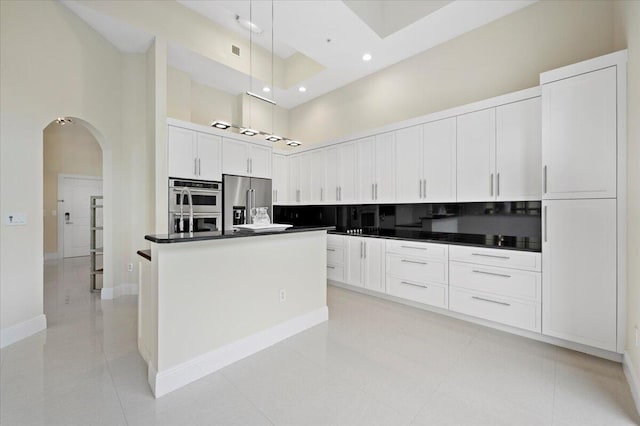 kitchen with appliances with stainless steel finishes, white cabinetry, a high ceiling, a kitchen island, and decorative light fixtures