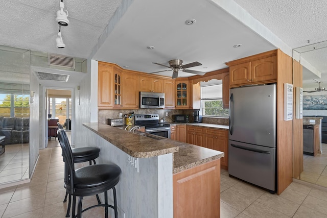 kitchen featuring light tile patterned floors, stainless steel appliances, tasteful backsplash, a kitchen bar, and kitchen peninsula