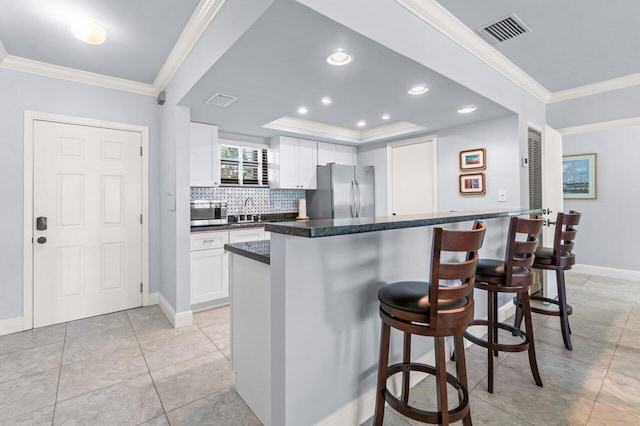 kitchen featuring a breakfast bar, white cabinetry, stainless steel appliances, ornamental molding, and a raised ceiling