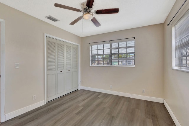 unfurnished bedroom featuring multiple windows, hardwood / wood-style floors, a closet, and ceiling fan