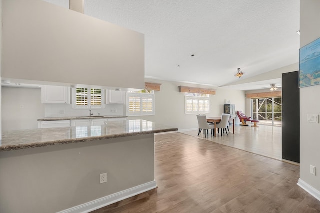 kitchen with white cabinetry, light stone counters, vaulted ceiling, ceiling fan, and hardwood / wood-style floors