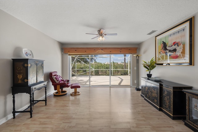 living area with ceiling fan, light hardwood / wood-style floors, and a textured ceiling