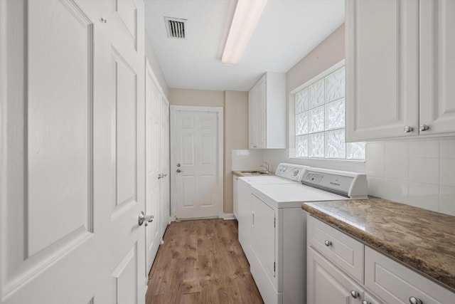 laundry area featuring cabinets, washing machine and dryer, and light hardwood / wood-style floors