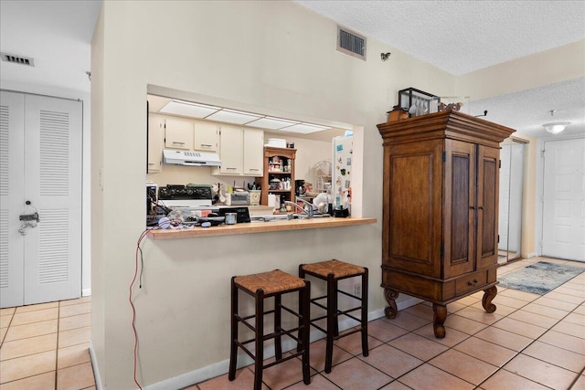 kitchen featuring a breakfast bar, light tile patterned floors, kitchen peninsula, a textured ceiling, and black / electric stove