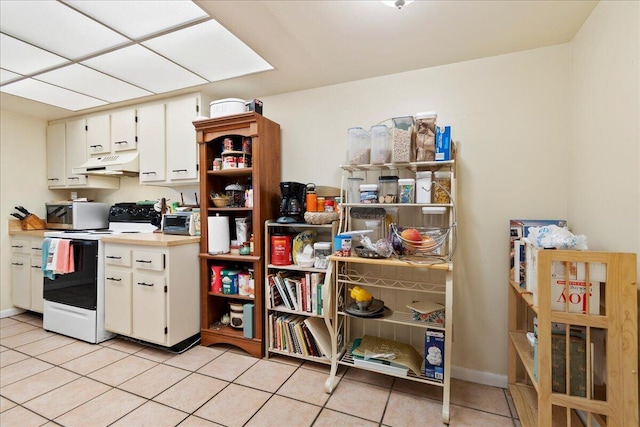 kitchen with electric range oven, light tile patterned floors, and white cabinets