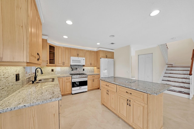 kitchen featuring sink, white appliances, light stone counters, a kitchen island, and light brown cabinetry