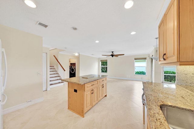 kitchen featuring a kitchen island, washer / clothes dryer, crown molding, light stone countertops, and light brown cabinets