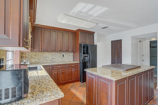 kitchen with decorative backsplash, a center island, light stone countertops, and black appliances