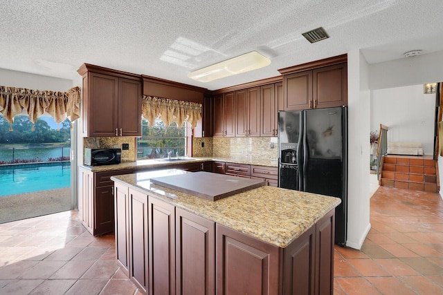 kitchen with sink, backsplash, a center island, light stone countertops, and black fridge