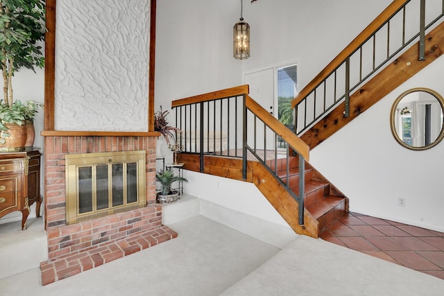 staircase with tile patterned flooring, a brick fireplace, a towering ceiling, and a notable chandelier