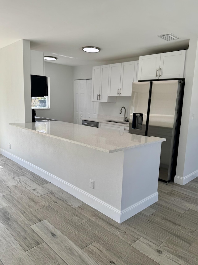 kitchen featuring light wood-type flooring, stainless steel fridge, sink, and white cabinets