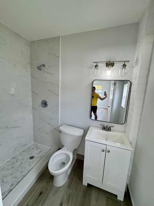 bathroom featuring vanity, toilet, wood-type flooring, and a tile shower