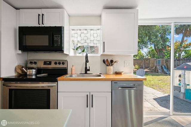 kitchen with wood counters, sink, white cabinetry, stainless steel appliances, and decorative backsplash