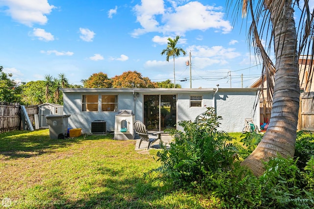 rear view of property with a storage shed, a yard, and central AC