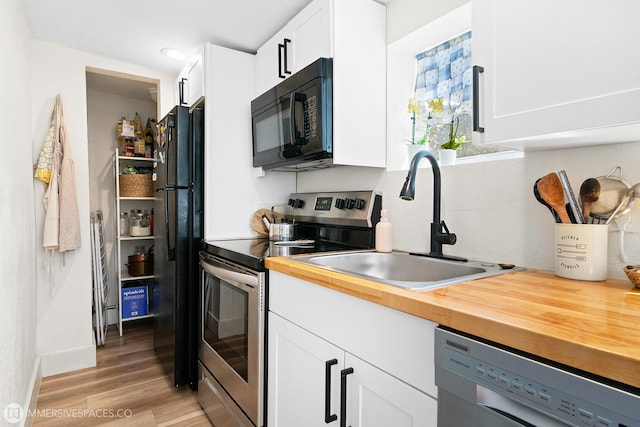 kitchen featuring butcher block countertops, sink, white cabinetry, light hardwood / wood-style flooring, and black appliances