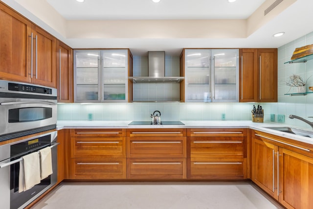 kitchen featuring wall chimney range hood, sink, double oven, backsplash, and black electric cooktop