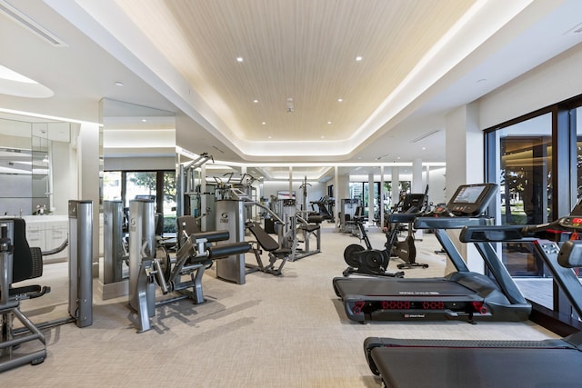 exercise room with light carpet, wooden ceiling, and a raised ceiling