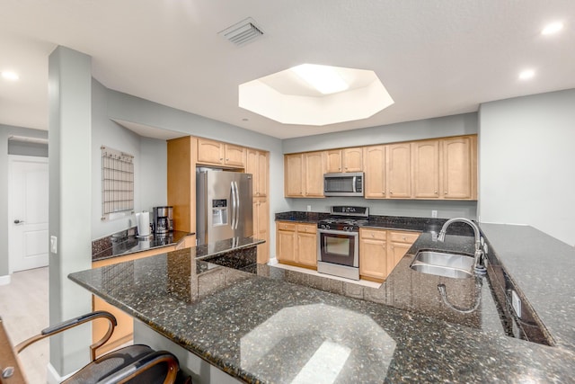 kitchen featuring sink, dark stone counters, kitchen peninsula, stainless steel appliances, and light brown cabinets