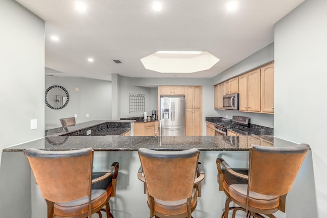 kitchen featuring appliances with stainless steel finishes, a breakfast bar, a skylight, kitchen peninsula, and light brown cabinets