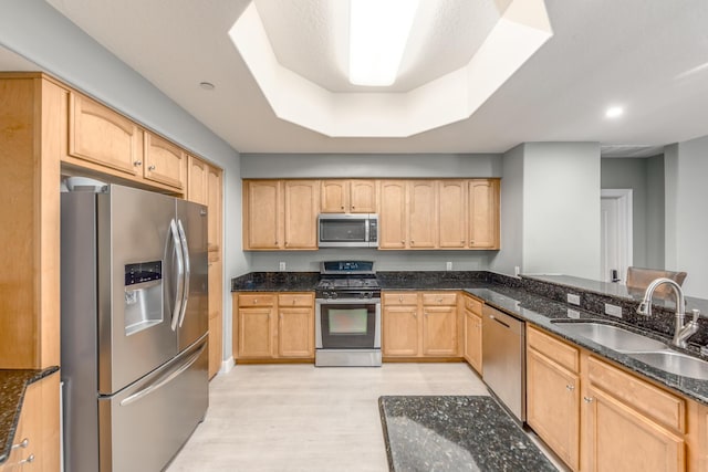 kitchen featuring light brown cabinetry, sink, dark stone countertops, a raised ceiling, and stainless steel appliances