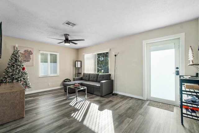 living room with dark wood-type flooring, ceiling fan, and a textured ceiling