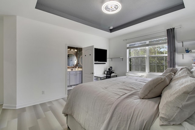 bedroom featuring a raised ceiling, light wood-type flooring, and ensuite bath