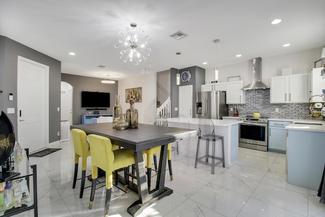 kitchen featuring wall chimney range hood, appliances with stainless steel finishes, white cabinets, a kitchen island, and decorative light fixtures