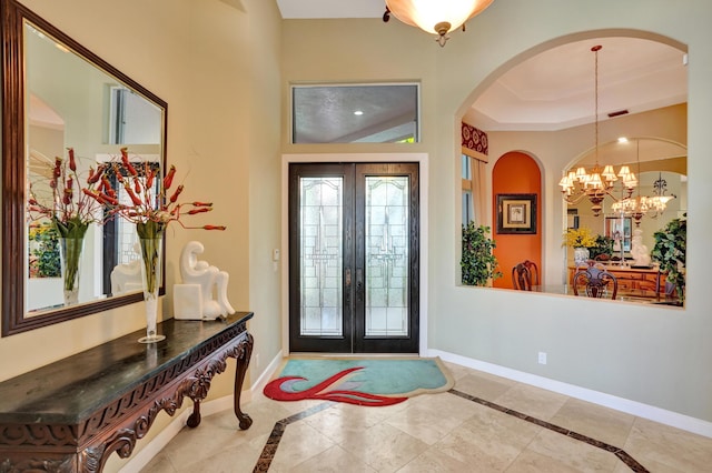 entryway with a raised ceiling, a notable chandelier, and french doors