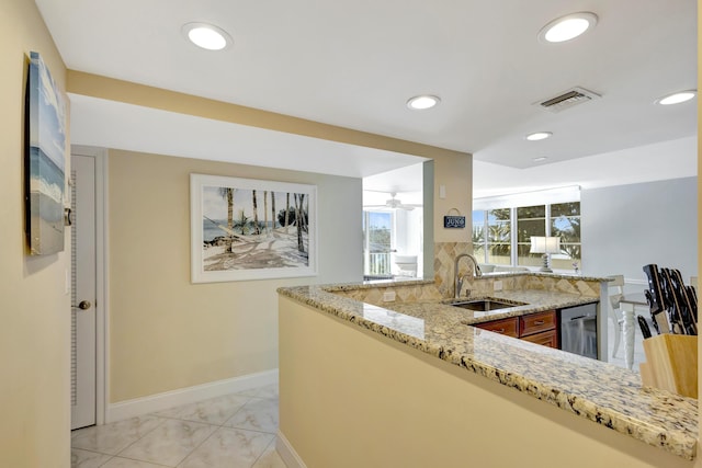 kitchen with stainless steel dishwasher, light stone countertops, sink, and kitchen peninsula