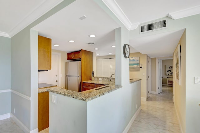 kitchen featuring light stone counters, ornamental molding, kitchen peninsula, and white fridge