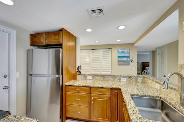 kitchen with light stone countertops, sink, and stainless steel refrigerator