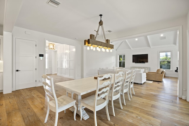 dining space with light hardwood / wood-style flooring and vaulted ceiling with beams