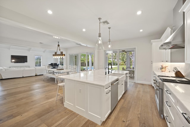 kitchen with sink, hanging light fixtures, stainless steel appliances, a kitchen island with sink, and white cabinets