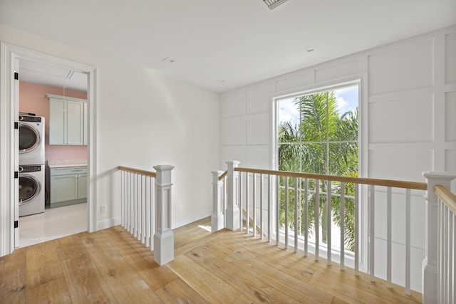 hall with stacked washer / drying machine and light hardwood / wood-style flooring