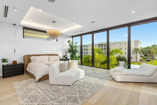 bedroom featuring light wood finished floors, visible vents, floor to ceiling windows, and a raised ceiling