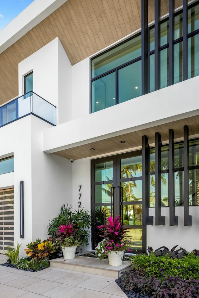 property entrance with a balcony, french doors, and stucco siding