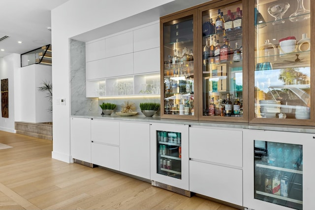 bar featuring a bar, beverage cooler, and light wood-type flooring