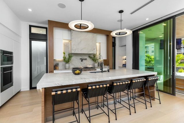 kitchen featuring a sink, white cabinetry, modern cabinets, light wood-type flooring, and backsplash