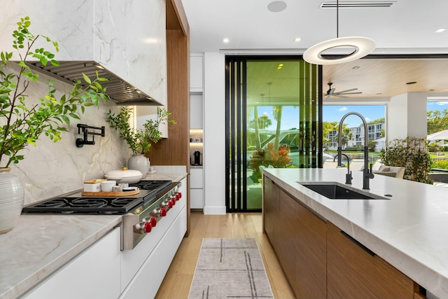 kitchen with a sink, modern cabinets, range hood, and light wood finished floors